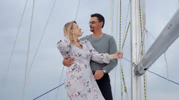 Full body of loving couple in summer clothes caressing on yacht while looking at each other