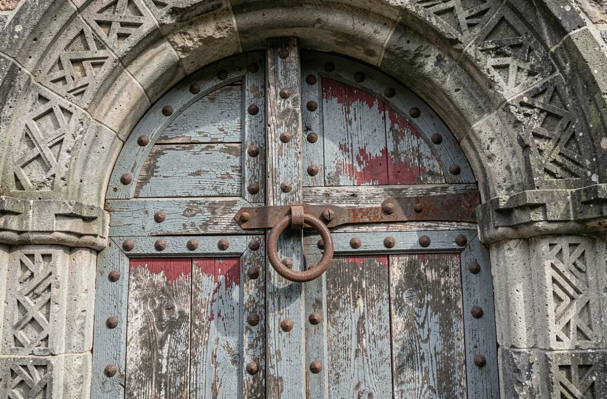 Détail d'une porte en bois ancienne avec ferrures forgées dans l'arche en pierre d'une église fortifiée de Transylvanie